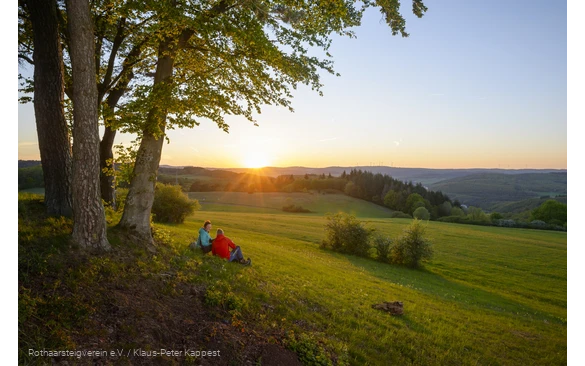 Wanderer sitzen auf einer Wiese und genießen den Sonnenuntergang