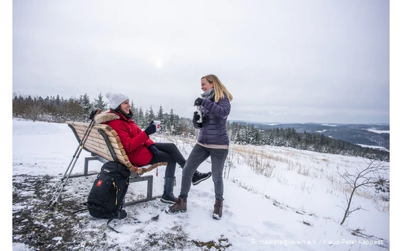 Zwei Frauen machen Pause an einer Rothaarsteig-Waldbank im Schnee