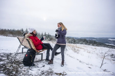 Zwei Frauen machen Pause an einer Rothaarsteig-Waldbank im Schnee