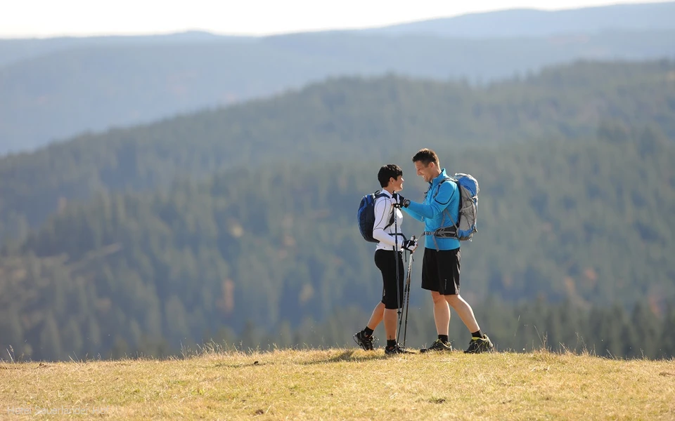 Zwei sportlich gekleidete Personen mit Speed Hiking-Ausrüstung vor einer Bergkulisse