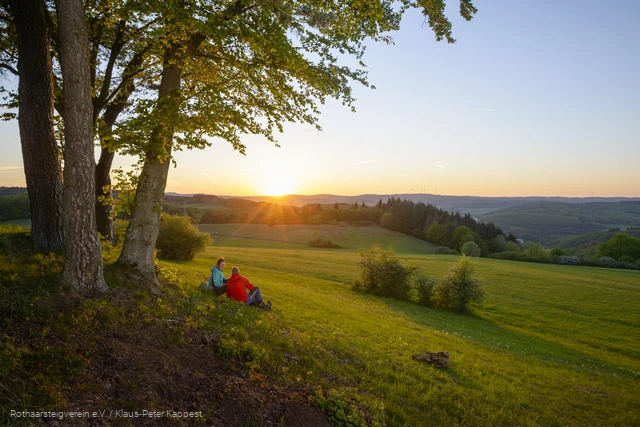 Wanderer sitzen auf einer Wiese und genießen den Sonnenuntergang